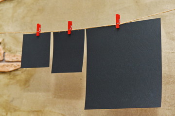 three black sheets of paper of different sizes with red clothespins on a rope