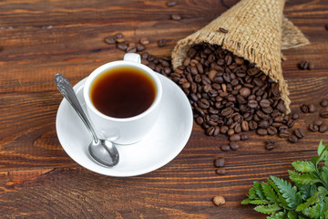 White cup of coffee. On a wooden background. Coffee beans are scattered all over the surface.