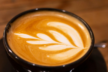 Black Cup of cappuccino on wooden table. Coffee cup of cappuccino with latte art. Cappuccino​ Coffee​ on dark table. Cappuccino, coffee, Coffee shop, coffee art, barista.