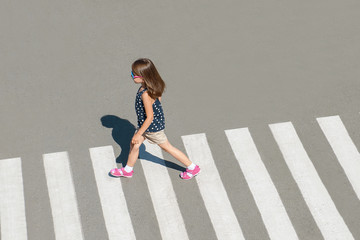 Stylish child in glasses, fashion clothes walking along summer city crosswalk. Kid on pedestrian side walk. Concept pedestrians passing a crosswalk. From top view. Shadow at zebra crossing