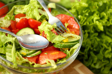 Silver fork and spoon in plate mixes salad fresh vegetables seasoned with olive oil. Raw food and vegetarian in modern society is popular concept.