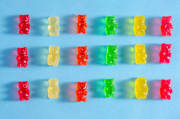 Delicious bright colored jelly bears on a blue background are laid out in the same order with hard shadows, top view