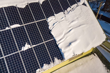 Close up surface of a house roof covered with solar panels in winter with snow on top. Energy efficiency and maintenance concept.