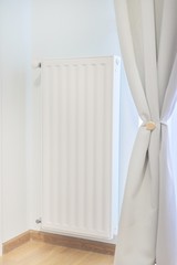 White heating radiator with thermostat in bright room interior