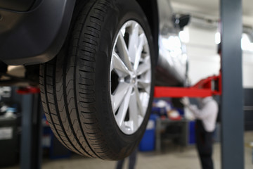 Close-up view of car all-season tire with aluminum rim. Mechanical lift for vehicle. Automobile service center or workshop concept. Professional auto maintenance