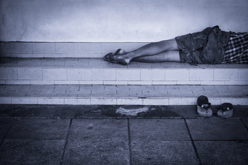 Homeless man dirty sleeps on the street in the shadow of the building.