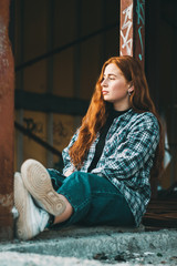 Stylish young beautiful girl in fashionable spring clothes with white sneakers sits on the asphalt