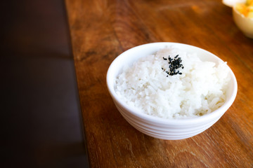 Rice in white cup on wood background and black sesame