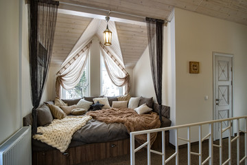 Interior of a modern house spacious hallway with big soft resting place. Contemporary wide sofa with many pillows and light window onder wooden loft ceiling.