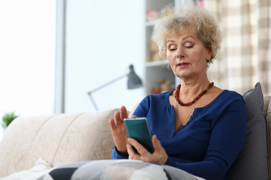 Portrait of senior woman using mobile phone. Attractive elderly female goes with the times. Copy space in left side. Cozy living room interior. Technology concept