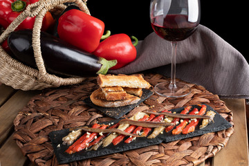 Escalivada with organic food vegetables in wicker basket on rustic wooden table with wine glass. vertical wiew.