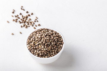 Raw organic unrefined hemp seeds in small white bowl on white concrete background.