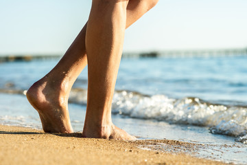 Close up of woman feet walking barefoot on sand beach in sea water. Vacation, travel and freedom...