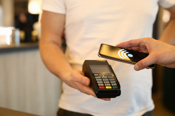 Close-up of customer person making payment via terminal and mobile phone in cafe. Pay by...