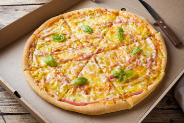Freshly baked pizza in a cardboard box on a wooden table.