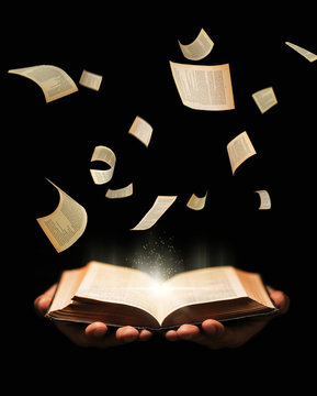 Man is holding book with flying pages and radiance light on black background. learing, reading, knowledge concept.