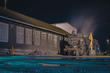 Old steam locomotive being fired up in front of a shed during the night. Romantic photo of a steam engine during the night. Vertical photo
