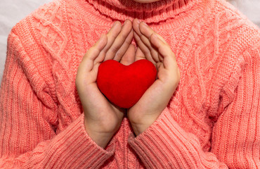 Children's hands hold a red heart on a background of a pink sweater. Symbol of love, family, hope....
