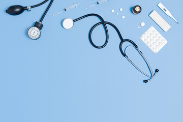 Medical blue background with different accessories: stethoscope, thermometer, syringe and tablets.