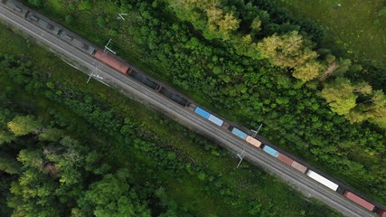 aerial view of a long freight train that goes along the tracks in the middle of the forest