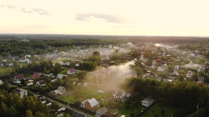 Aerial shot of beautiful countryside village in the morning sunlight, with mist floating on the farm land field. Cooking smoke curls up.