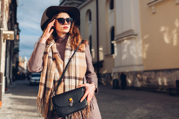 Obraz premium Street female fashion. Portrait of stylish young woman wearing hat glasses holding purse outdoors. Spring accessories