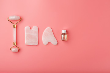 Gua sha massage tool made of natural pink Quartz-roller, jade stone and oil, on a pink background for face and body care. Part of traditional Chinese medicine