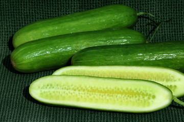 A group of cucumbers on a dark green rustic background. There are three whole cucumbers and one sliced in half.