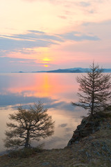 Fototapeta na wymiar Baikal Lake in the spring at dawn. The rising sun over the Strait of Small Sea. Beautiful quiet landscape with larch trees on the shore in the early morning. Natural background