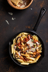 Pasta with meat ragout, grilled aubergines and parmesan cheese in cast iron pan on dark rustic background.