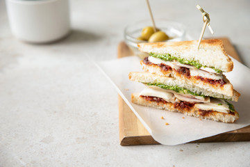 Sandwich with chicken breast, dried tomatoes, mozzarella and pesto with olives on background.