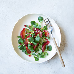 Fresh salad with blood orange, lettuce, pomegranate seeds and pistachios.