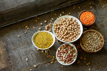 Diet and healthy eating concept, vegan protein source. Raw of legumes (chickpeas, red lentils, canadian lentils, beans, bulgur) on wooden table. Copy space.