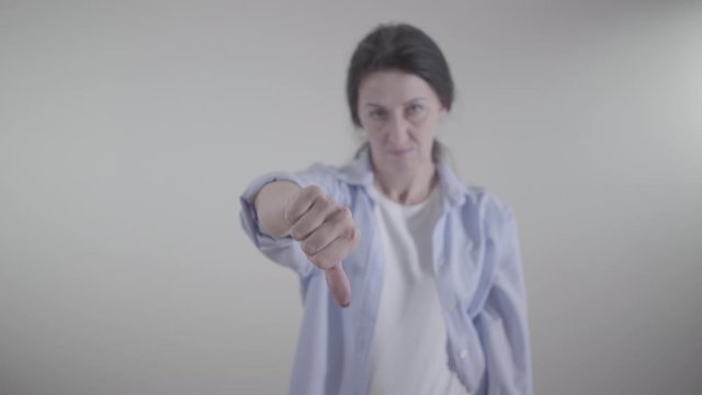 Close-up of female hand showing thumb down. Blurred Caucasian woman gesturing no by shaking head at the background. Disapproval, negativism, objection concept.