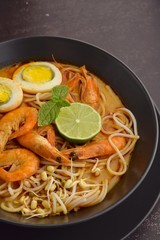 Laksa noodle soup with prawn, egg and bean sprouts garnish with lime and mint