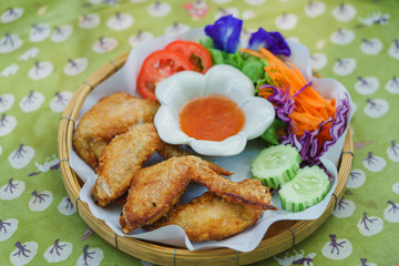 Delicious crispy fried chicken with Thai dipping sauce and tomato .cucumber vegetable on tracing paper in basket.