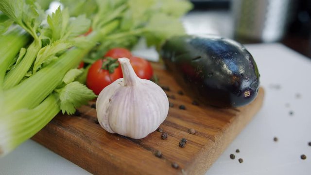 Close-up of fresh ripe vegetables tomatoes, celery, eggplant and garlic on wooden chopping board in kitchen. Cooking meals, salad and vegan diet concept.