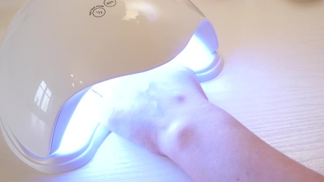 The girl dries the shellac in the lamp