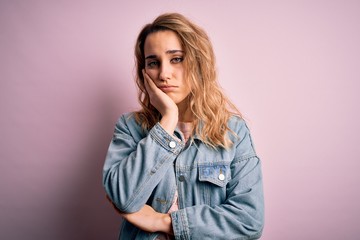 Young beautiful blonde woman wearing casual denim jacket standing over pink background thinking...