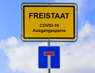 Ausgangssperre wegen Coronavirus steht auf Ortsschild für den Freistaat