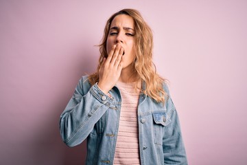 Young beautiful blonde woman wearing casual denim jacket standing over pink background bored yawning tired covering mouth with hand. Restless and sleepiness.