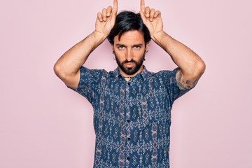 Young handsome hispanic bohemian man wearing hippie style over pink background doing funny gesture...