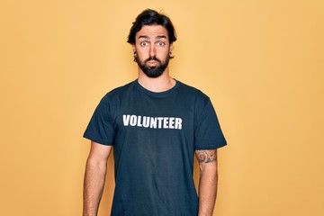 Young handsome hispanic volunteer man wearing volunteering t-shirt as social care puffing cheeks...