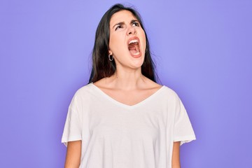 Fototapeta premium Young beautiful brunette woman wearing casual white t-shirt over purple background angry and mad screaming frustrated and furious, shouting with anger. Rage and aggressive concept.