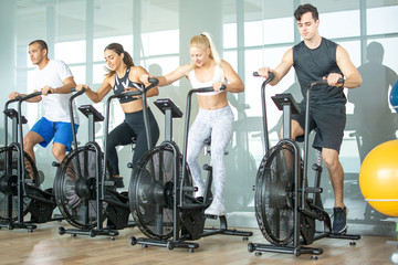 Group of young people doing exercises on elliptical machine at gym