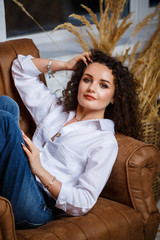 Beautiful young girl model with curls posing. She is wearing a white shirt and jeans.