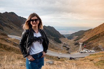 Naklejka premium Young beautiful girl or woman portrait standing in a mountain landscape. Travel for fun. Large valley in background with long roads.