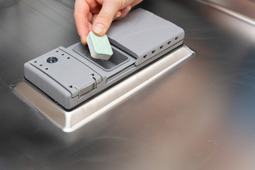 A teenager places a cube of powder in a special dishwasher monument.