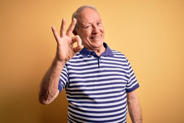 Naklejka premium Grey haired senior man wearing casual navy striped t-shirt standing over yellow background smiling positive doing ok sign with hand and fingers. Successful expression.