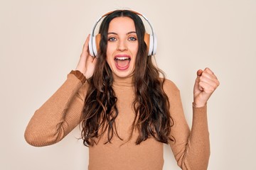 Young beautiful woman with blue eyes listening to music and dancing using headphones screaming proud and celebrating victory and success very excited, cheering emotion